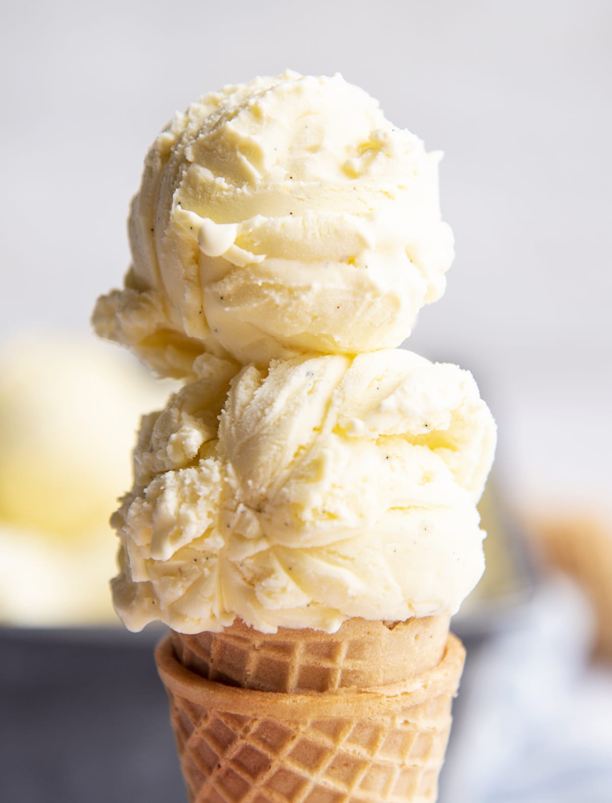A close up of a french vanilla ice cream cone with two scoops on top.