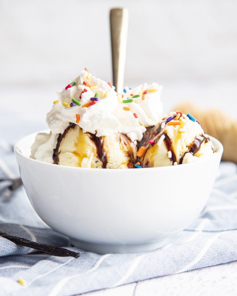 A bowl of French vanilla ice cream topped with caramel sauce, hot fudge, whipped cream, and sprinkles.