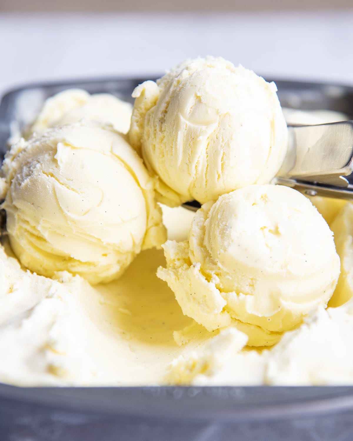 A close up of three scoops of homemade vanilla bean ice cream in a container of the ice cream.