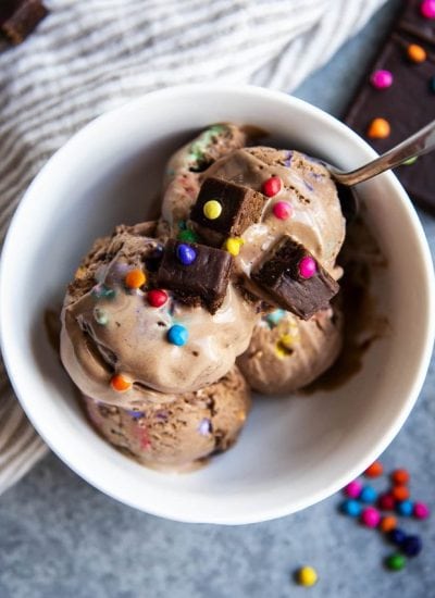 An overhead photo of a bowl of chocolate ice cream full of cosmic brownies and rainbow candy coated chips.