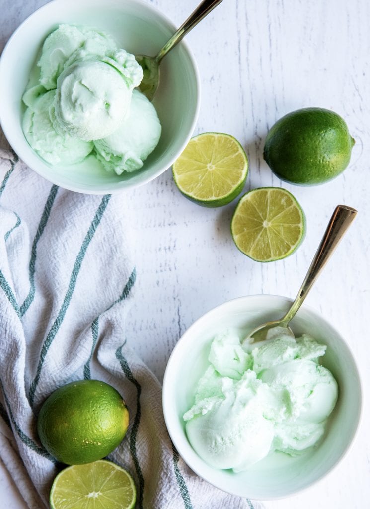 An overhead photo of two bowls of green lime sherbet, with fresh limes next to them.