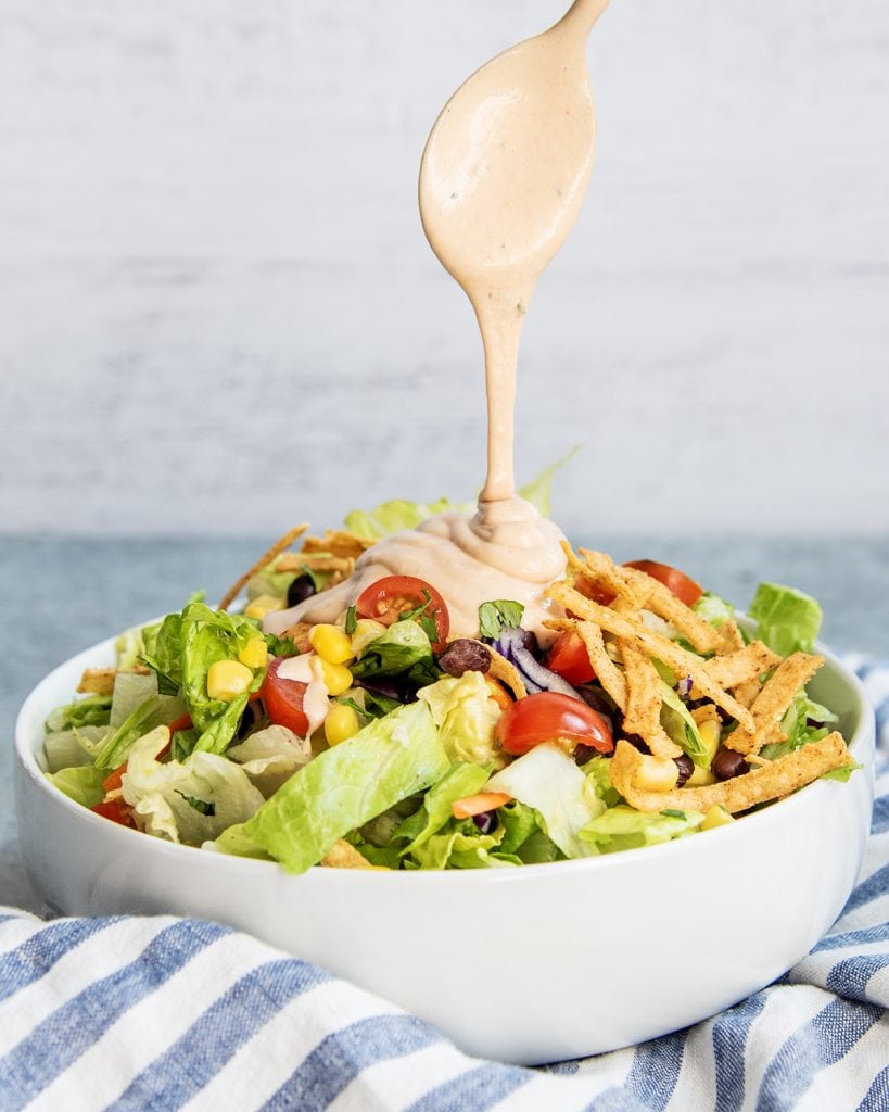 A spoon drizzling BBQ Ranch Dressing on a green salad.