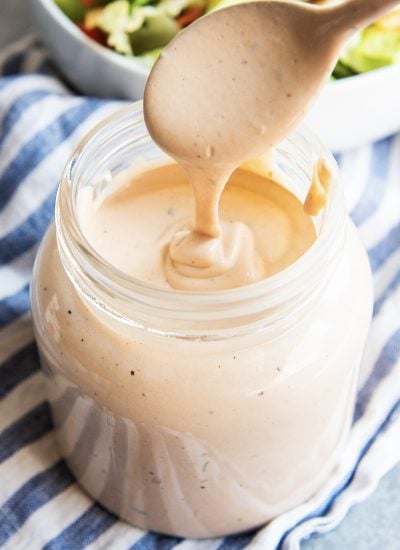 A spoon drizzling BBQ Ranch dressing back into a glass jar of the dressing.