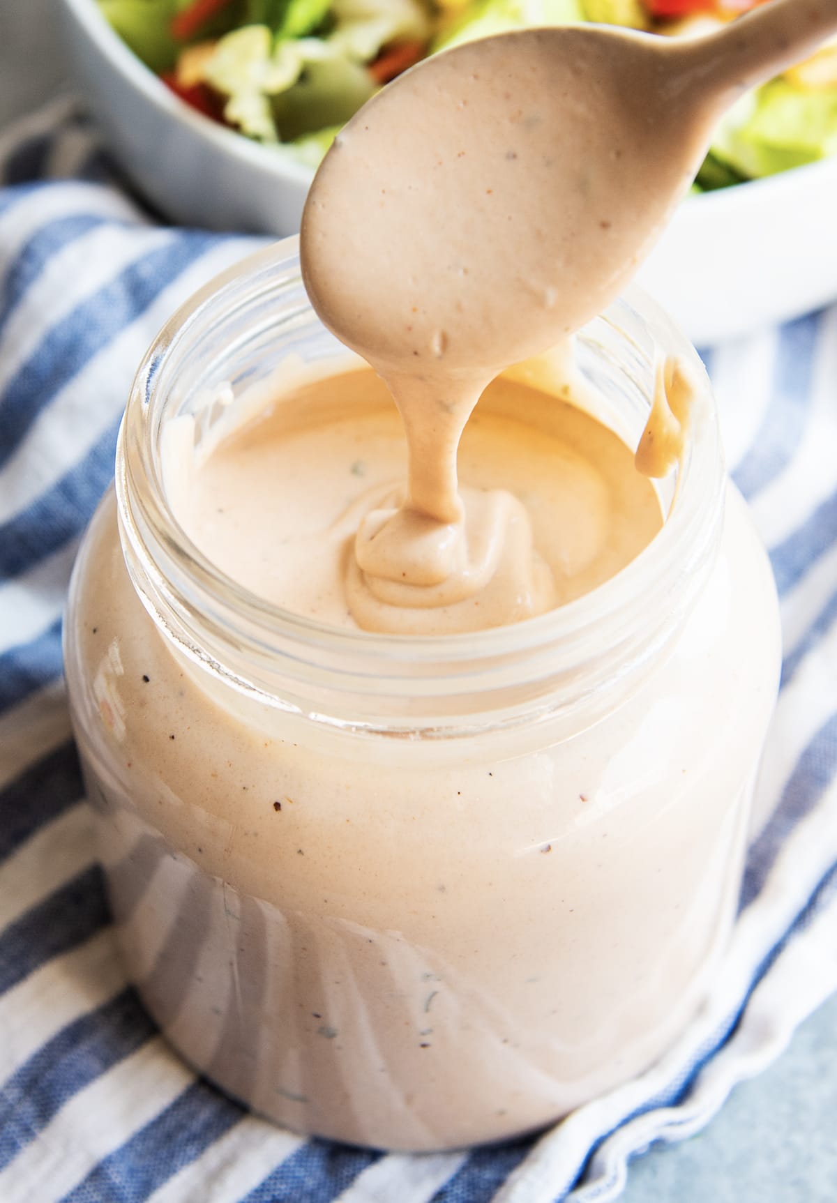 A spoon drizzling BBQ Ranch dressing back into a glass jar of the dressing.