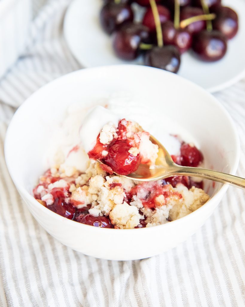 A spoonful of cherry cobbler above a bowl of it.
