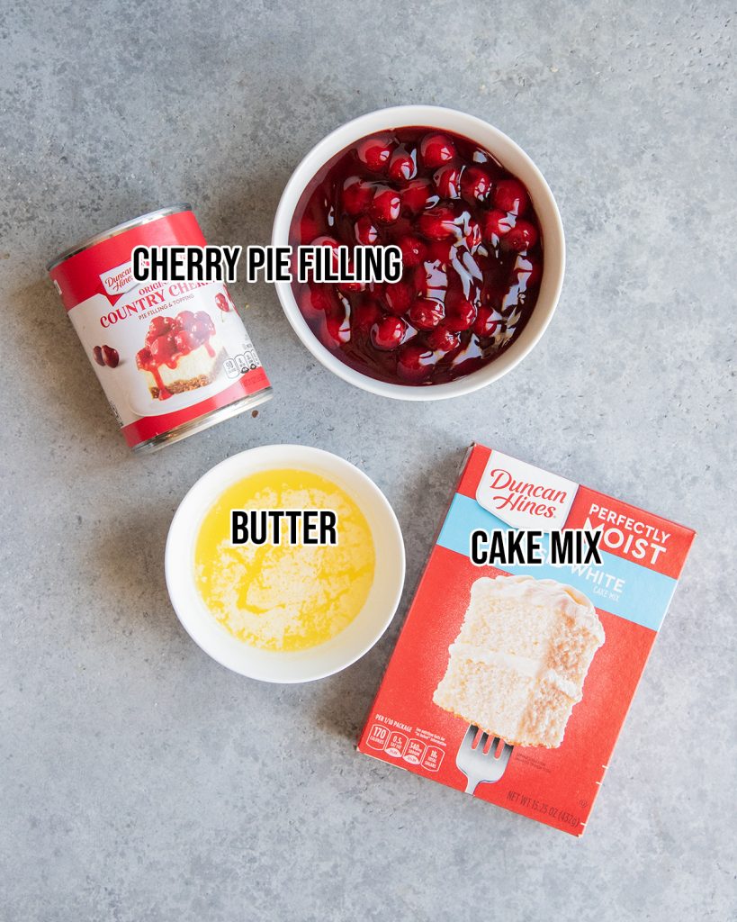 An overhead photo of the three ingredients needed to make cherry cobbler, cherry pie filling, salted butter, and white cake mix.