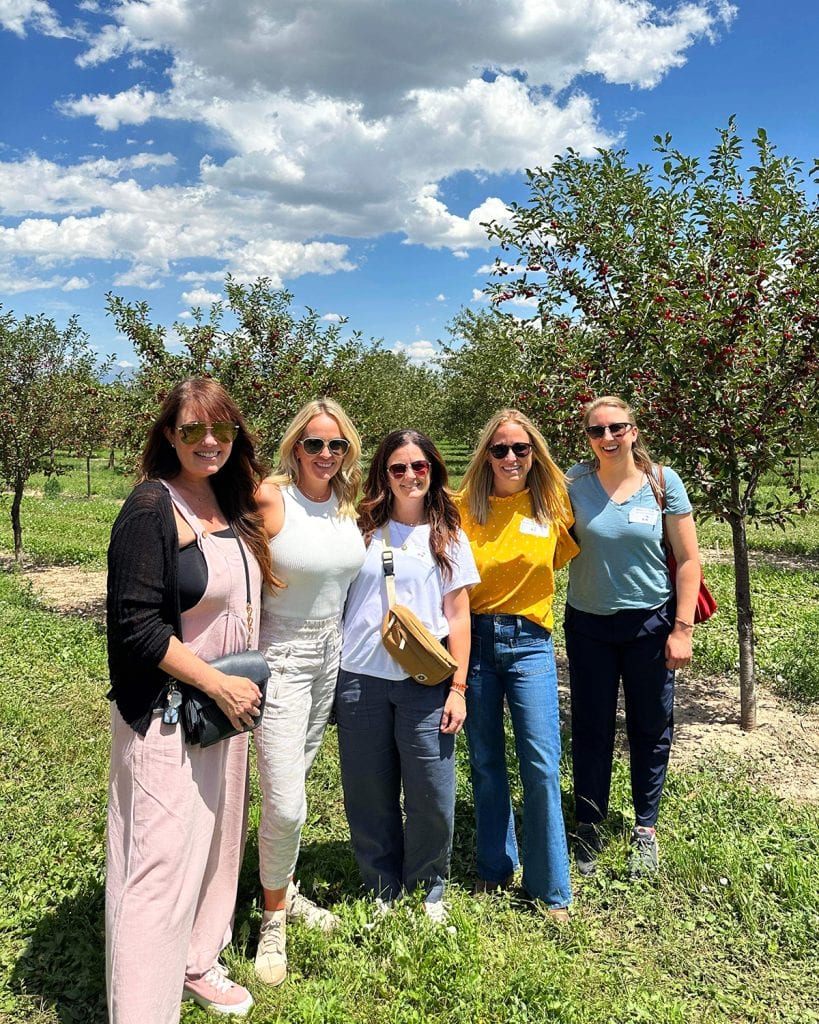 Five women in a row standing in a row of cherry trees.