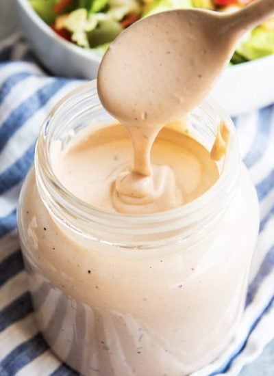 A spoon drizzling BBQ Ranch dressing back into a glass jar of the dressing.