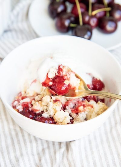 A spoonful of cherry cobbler above a bowl of it.