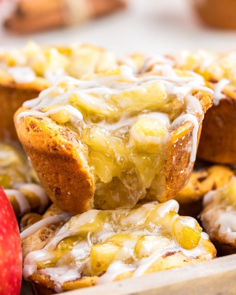 A cinnamon roll apple pie cup with a bite out of it, showing the apple pie filling in the middle.