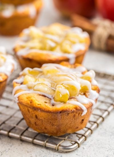 A cinnamon roll apple pie cup full of apple pie filling and drizzled with cinnamon roll icing on a cooling rack.