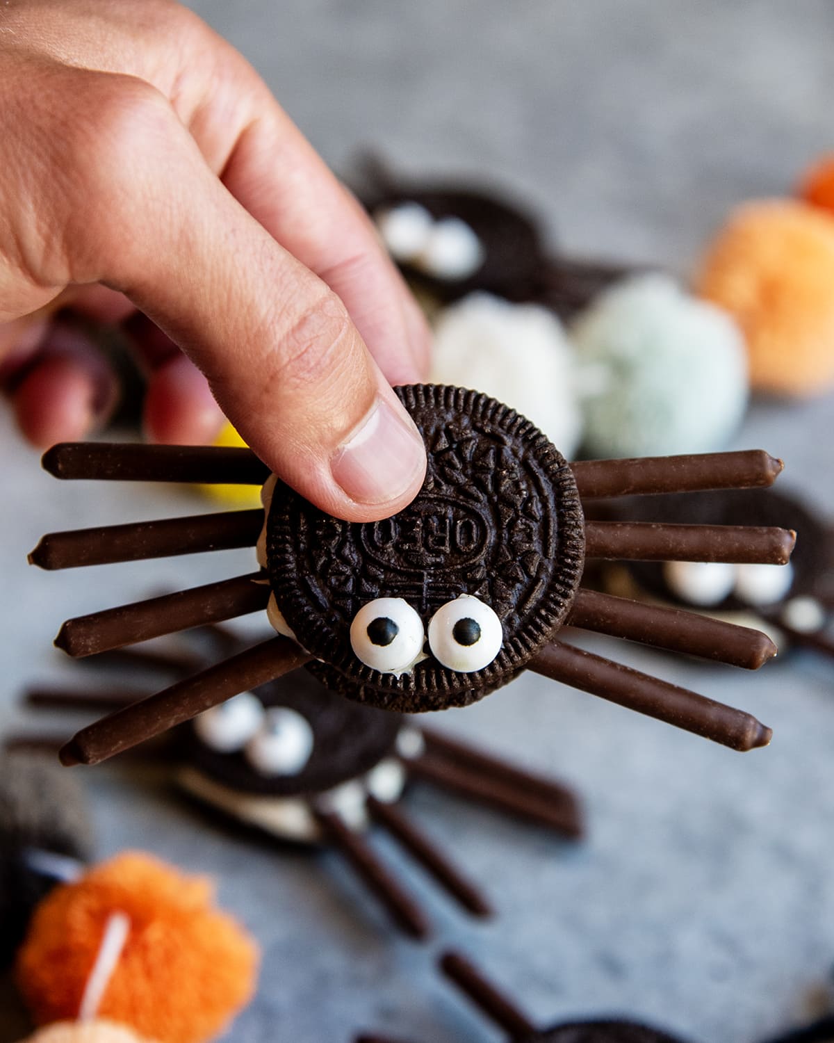 A hand holding a chocolate Oreo spider with 4 chocolate pocky legs on each side.
