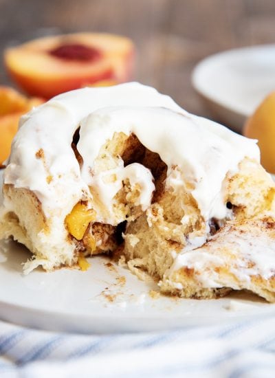 A peach cinnamon roll on a plate, that is cut into showing peaches and the gooey center.