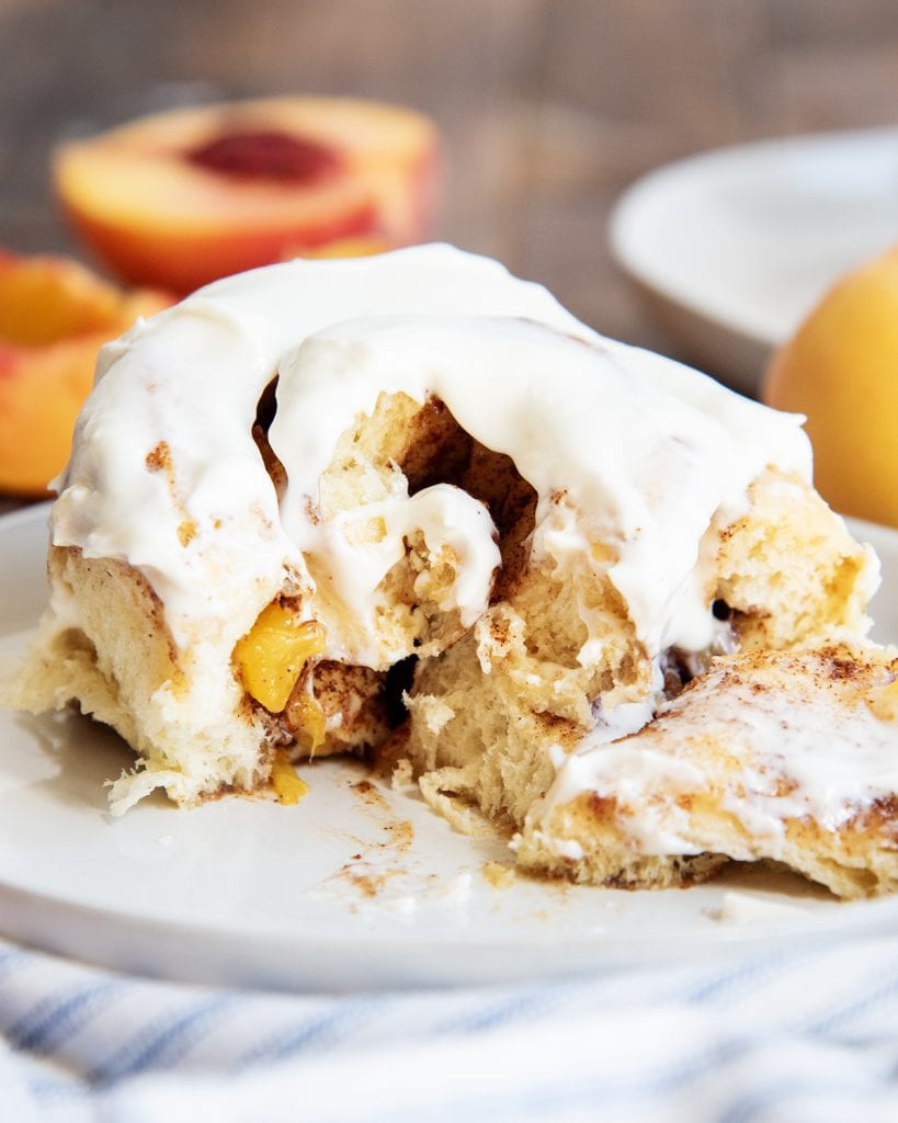 A peach cinnamon roll on a plate, that is cut into showing peaches and the gooey center.