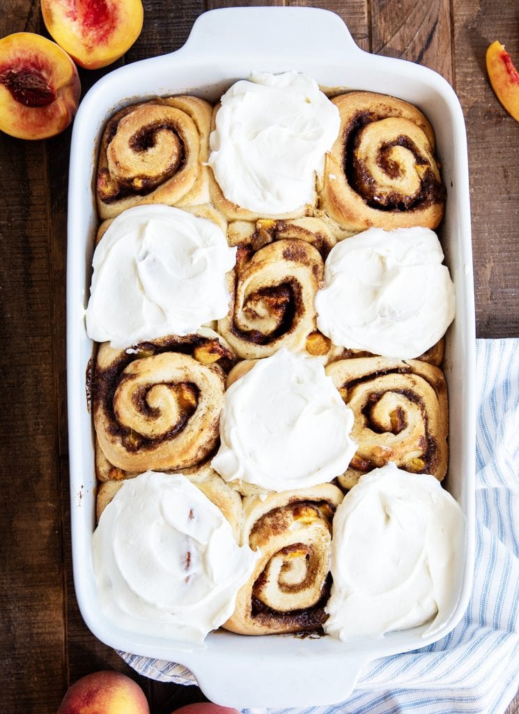 An overhead photo of a pan of peach cinnamon rolls. Half of them are topped with a white frosting.