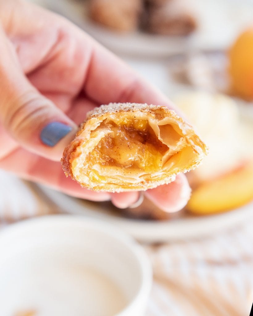 A hand holding a peach cobbler egg roll with a bite out of it.