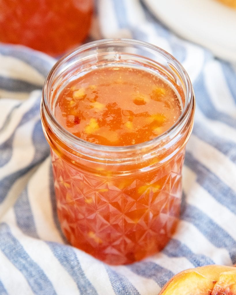 A small glass jar full of peach freezer jam without a lid on it.