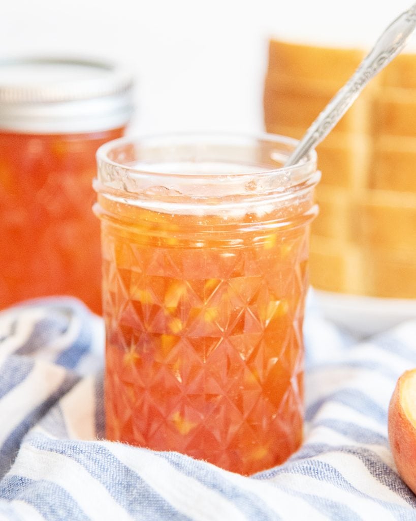 A jar of peach freezer with a spoon it it.