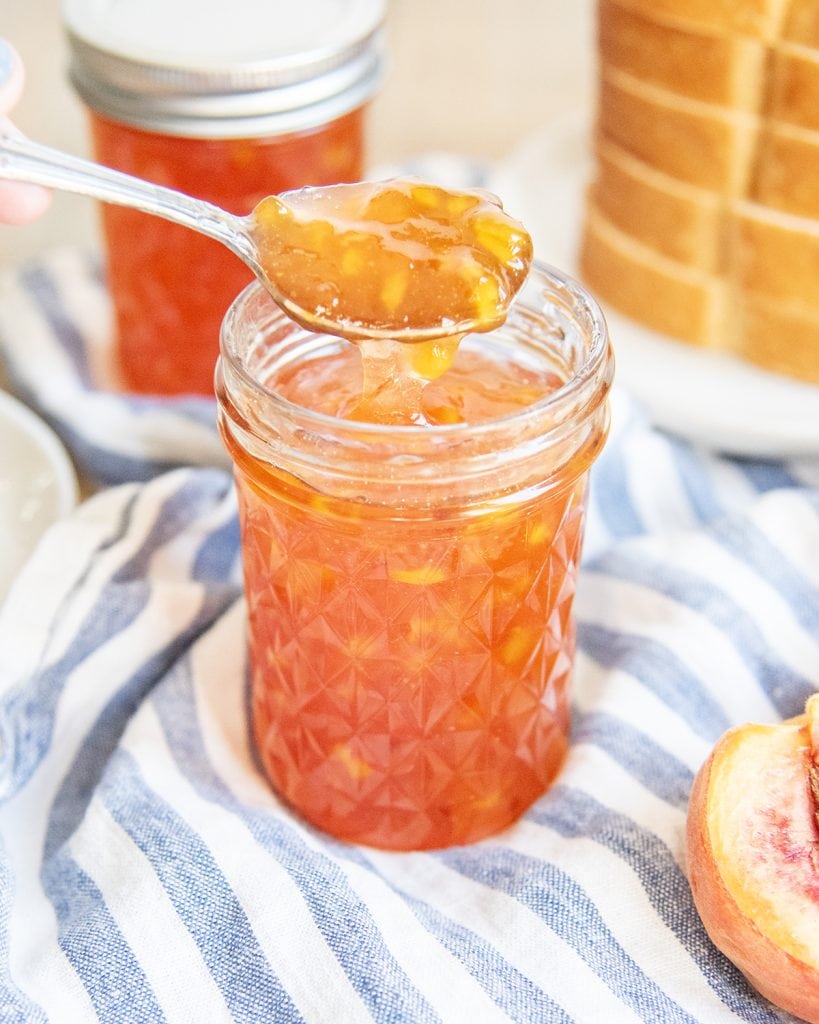 A spoon lifting peach jam out of a jar of it.