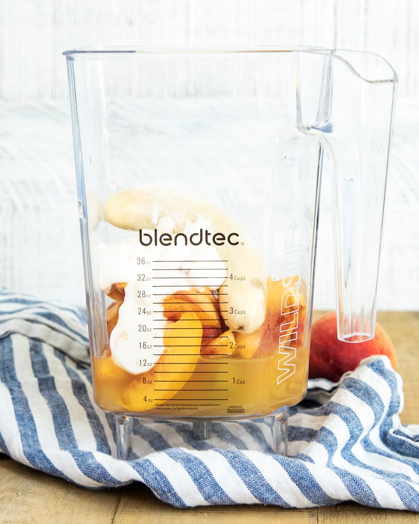 A blender with frozen peaches, peach juice, yogurt, and a banana in it.