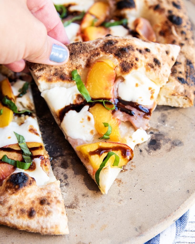A slice of peach pizza topped with balsamic glaze, being held in a hand.