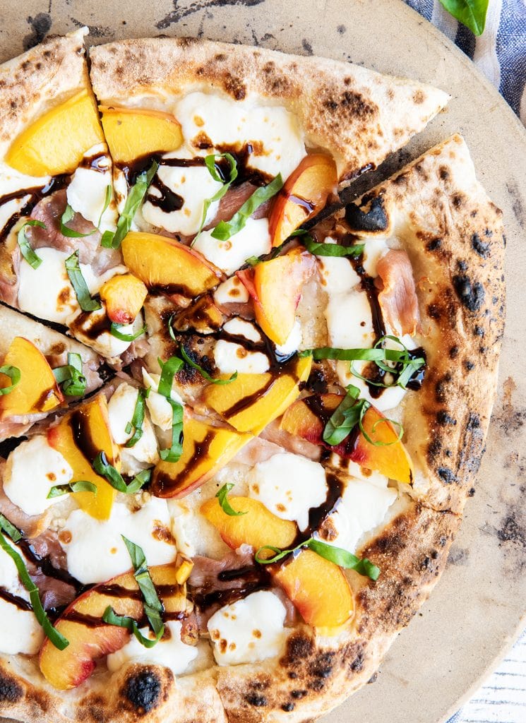 An overhead photo of a peach and prosciutto pizza topped with balsamic glaze and fresh basil, cut into slices.