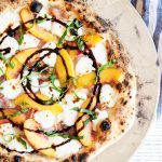 A photo of peach pizza topped with fresh basil and a circular balsamic glaze drizzle.