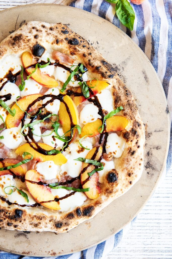 A photo of peach pizza topped with fresh basil and a circular balsamic glaze drizzle.
