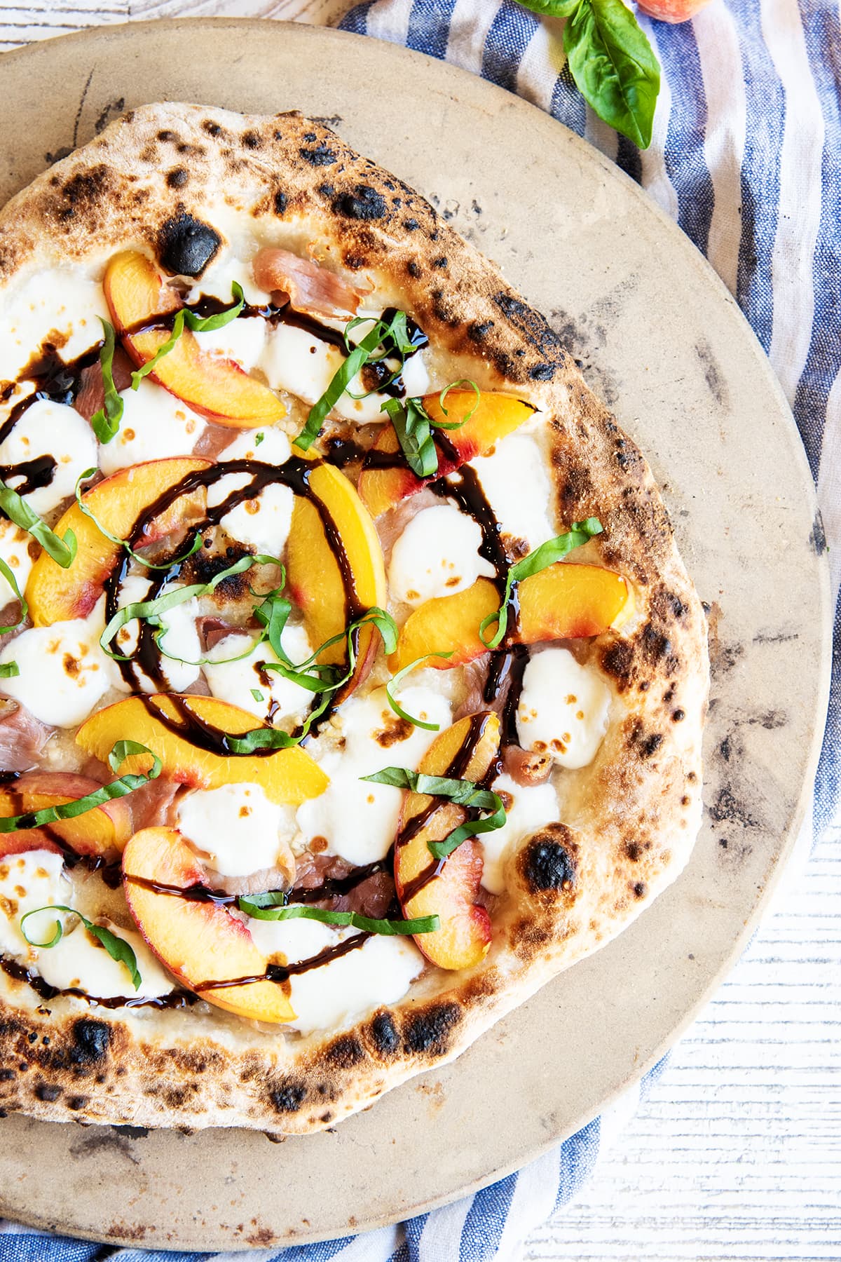 A photo of peach pizza topped with fresh basil and a circular balsamic glaze drizzle.