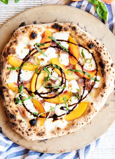 An overhead photo of a prosciutto and peach pizza topped with melted mozzarella, balsamic glaze, and fresh basil.