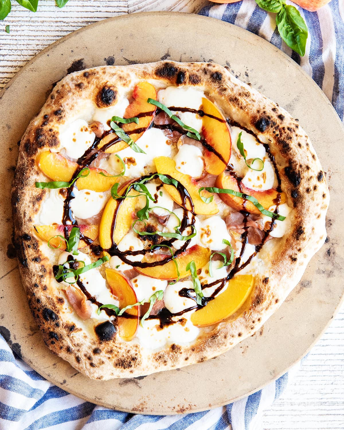 An overhead photo of a prosciutto and peach pizza topped with melted mozzarella, balsamic glaze, and fresh basil.