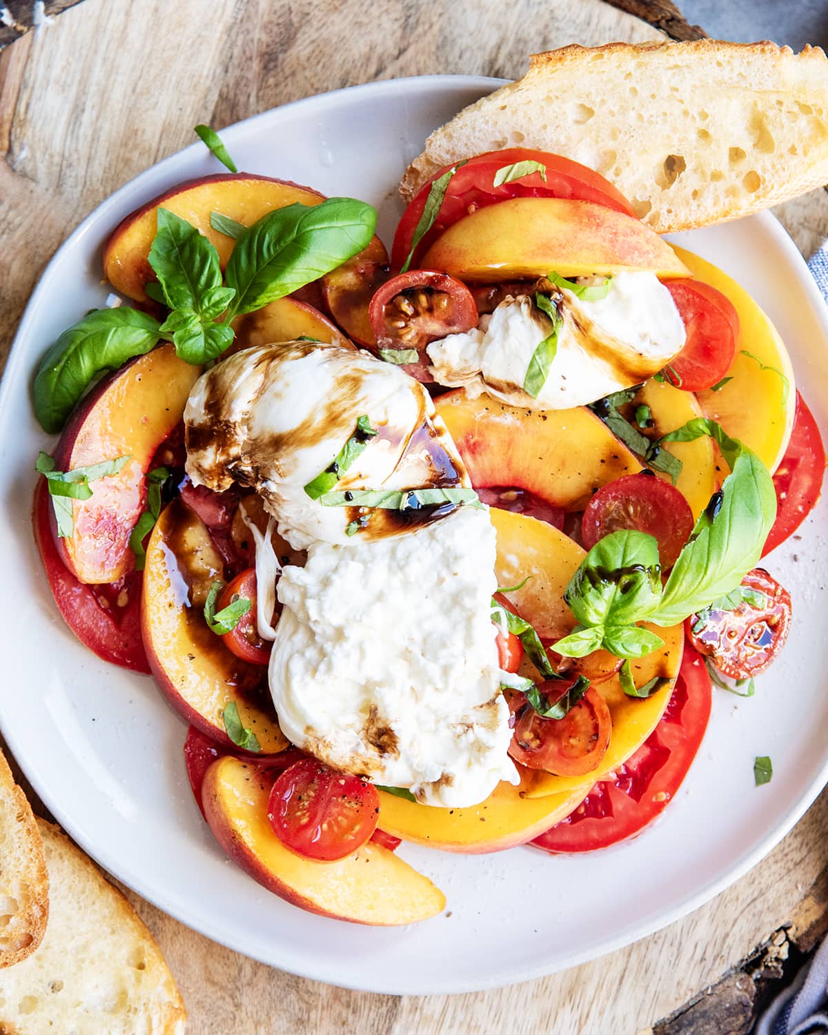 A peach and tomato burrata salad on a plate, with the burrata cut into, and topped with balsamic glaze.