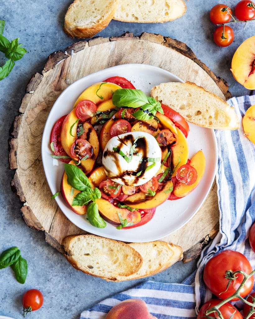 An overhead photo of a plate of tomato peach burrata on a plate with toasted bread next to it.