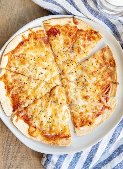 An overhead photo of a sliced tortilla pizza topped with Italian seasonings.