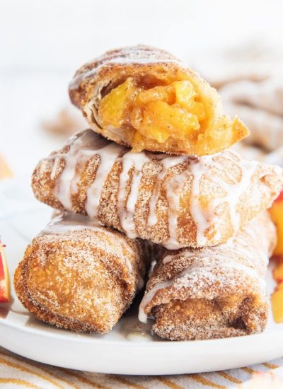 A stack of peach cobbler egg rolls, and the top one is cut open showing the peach filling.