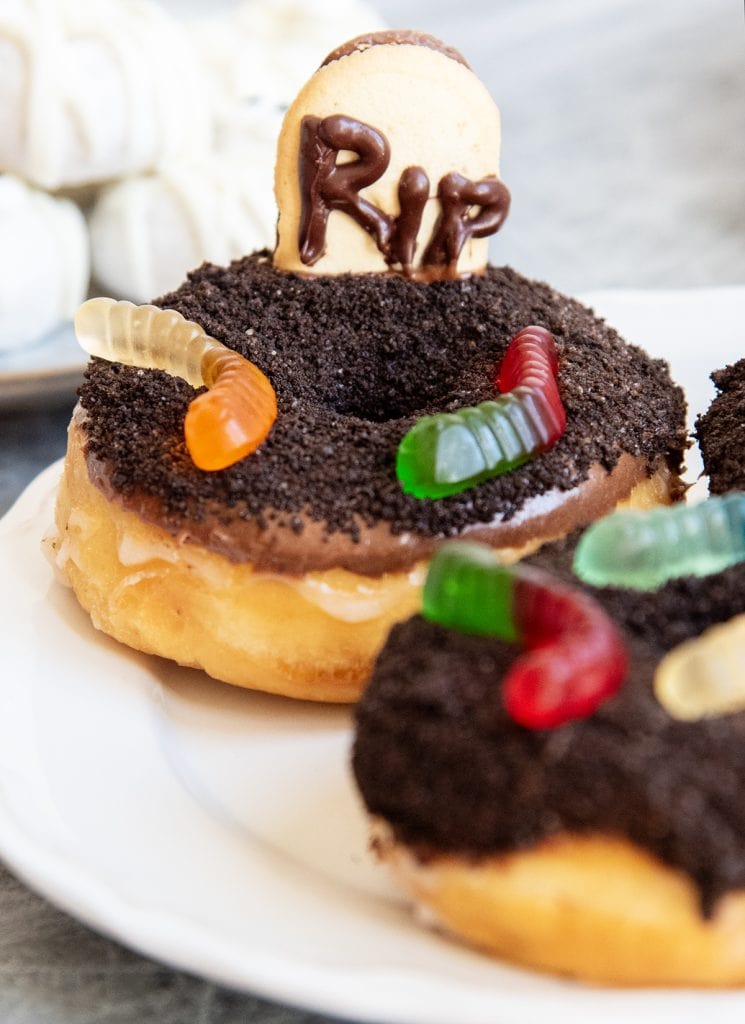 A graveyard donut topped with Oreo crumbs for dirt, and gummy worms, and a cookie tombstone.