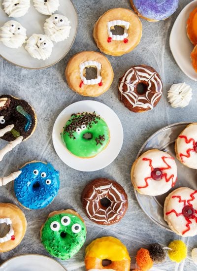 An overhead view of different types of Halloween decorated donuts, mummy donuts, spider web donuts, monster donuts, and eyeball donuts.