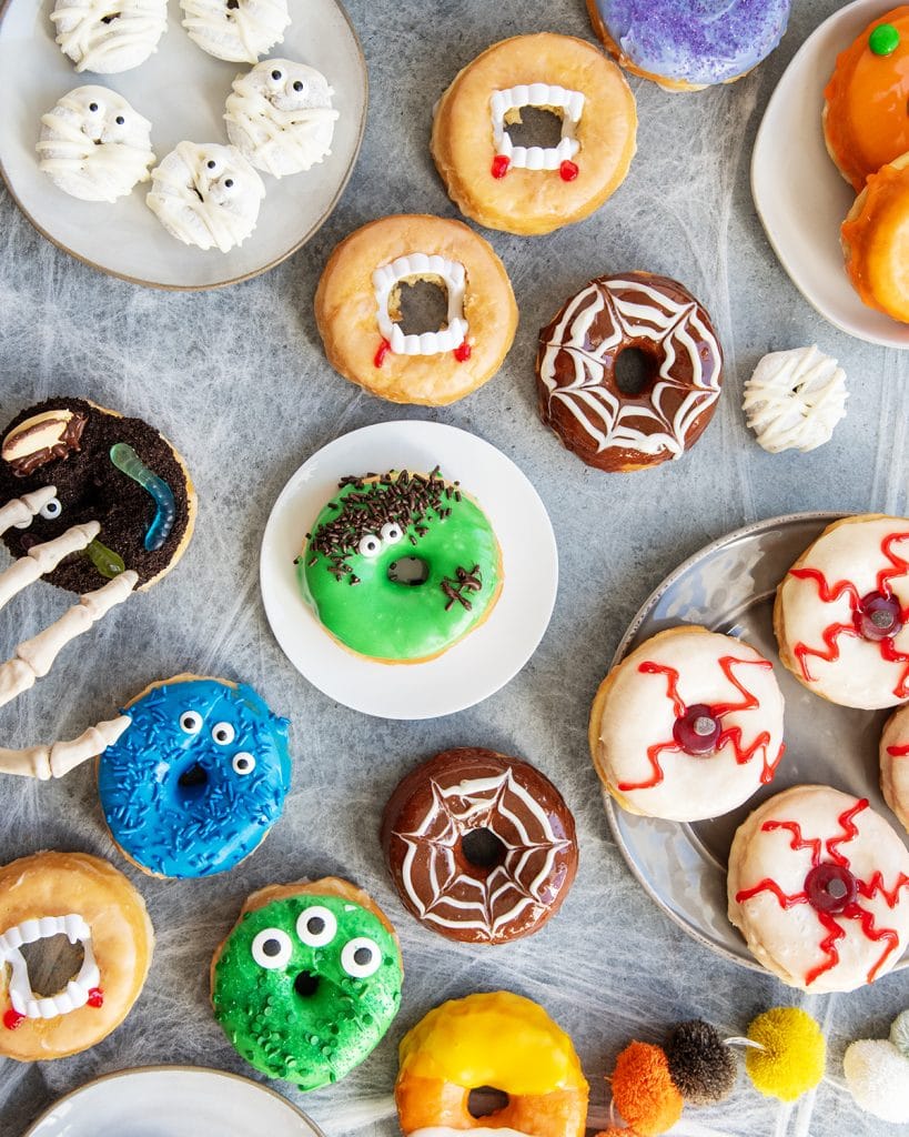 An overhead view of different types of Halloween decorated donuts, mummy donuts, spider web donuts, monster donuts, and eyeball donuts.