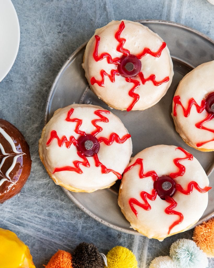 A plate of 4 creepy eyeball donuts topped with red gel, and a lifesaver gummy eye.