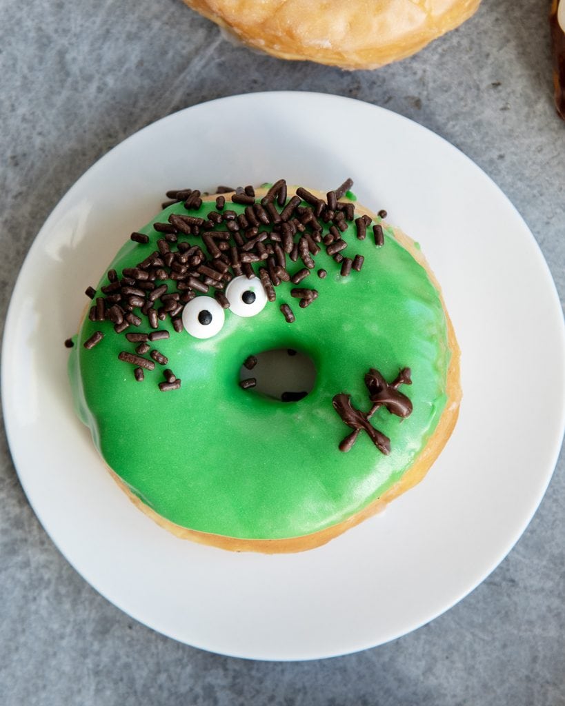 A frankenstein decorated green donut on a plate.