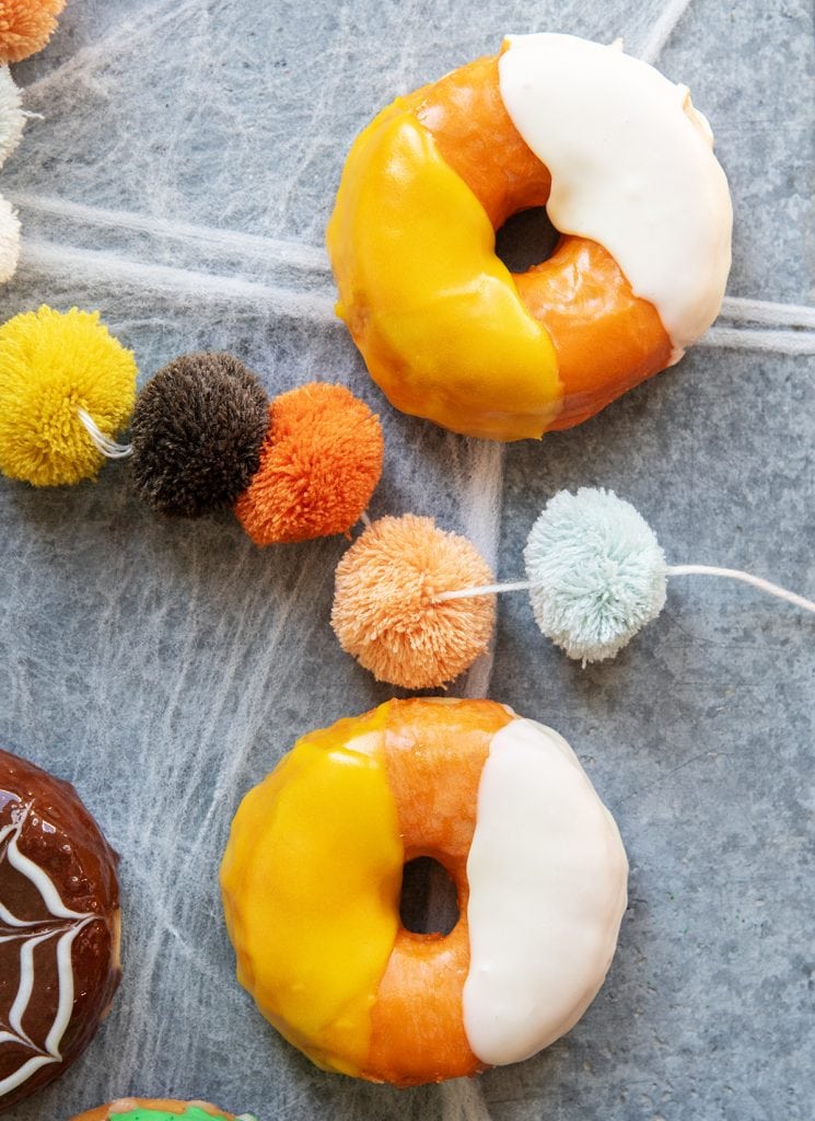 Two donuts decorated with yellow, orange, and white to look like the colors of candy corn.