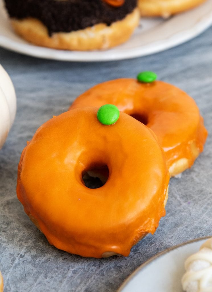 Two orange donuts topped with a green m&m to look like pumpkins.