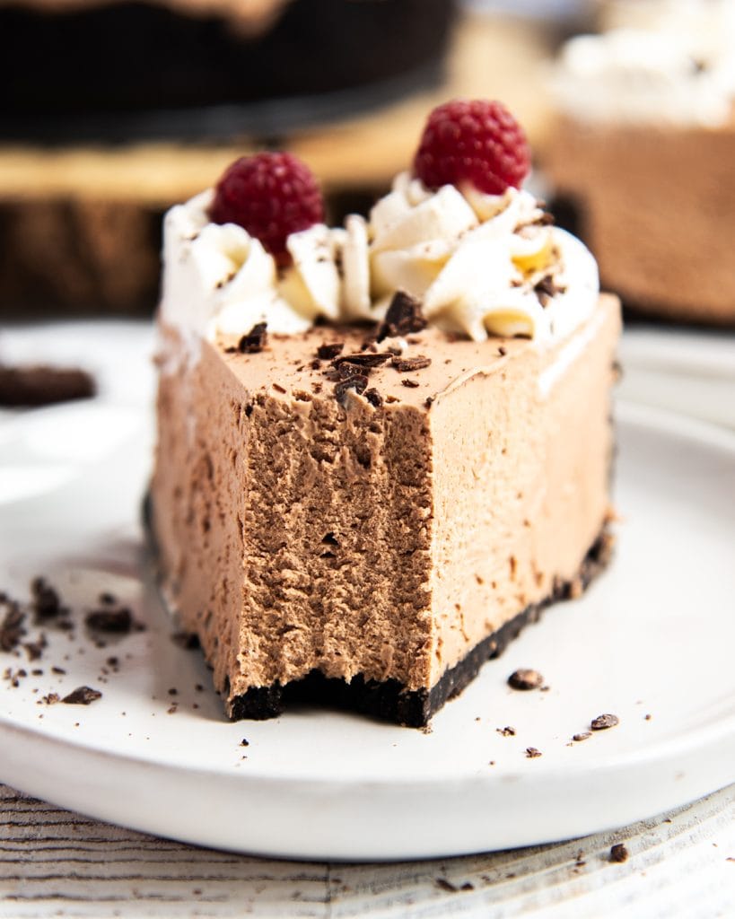 A slice of chocolate cheesecake on a plate with a bite taken out of it.