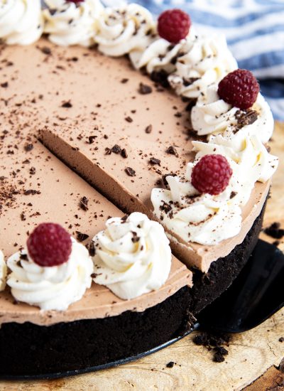 A no bake chocolate cheesecake on a wooden board, topped with dollops of whipped cream.