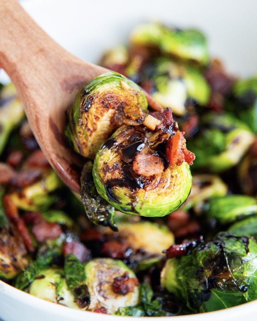 A wooden spoon with bacon brussel sprouts on them.
