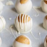 Rows of Biscoff cookie balls on a cookie sheet, drizzled with white chocolate.