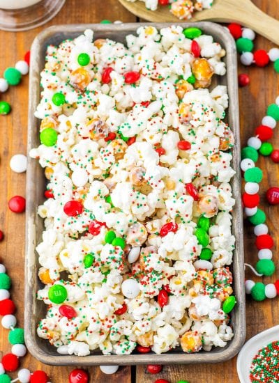 A pan of Christmas popcorn covered in white chocolate, and red, white and green round sprinkles.