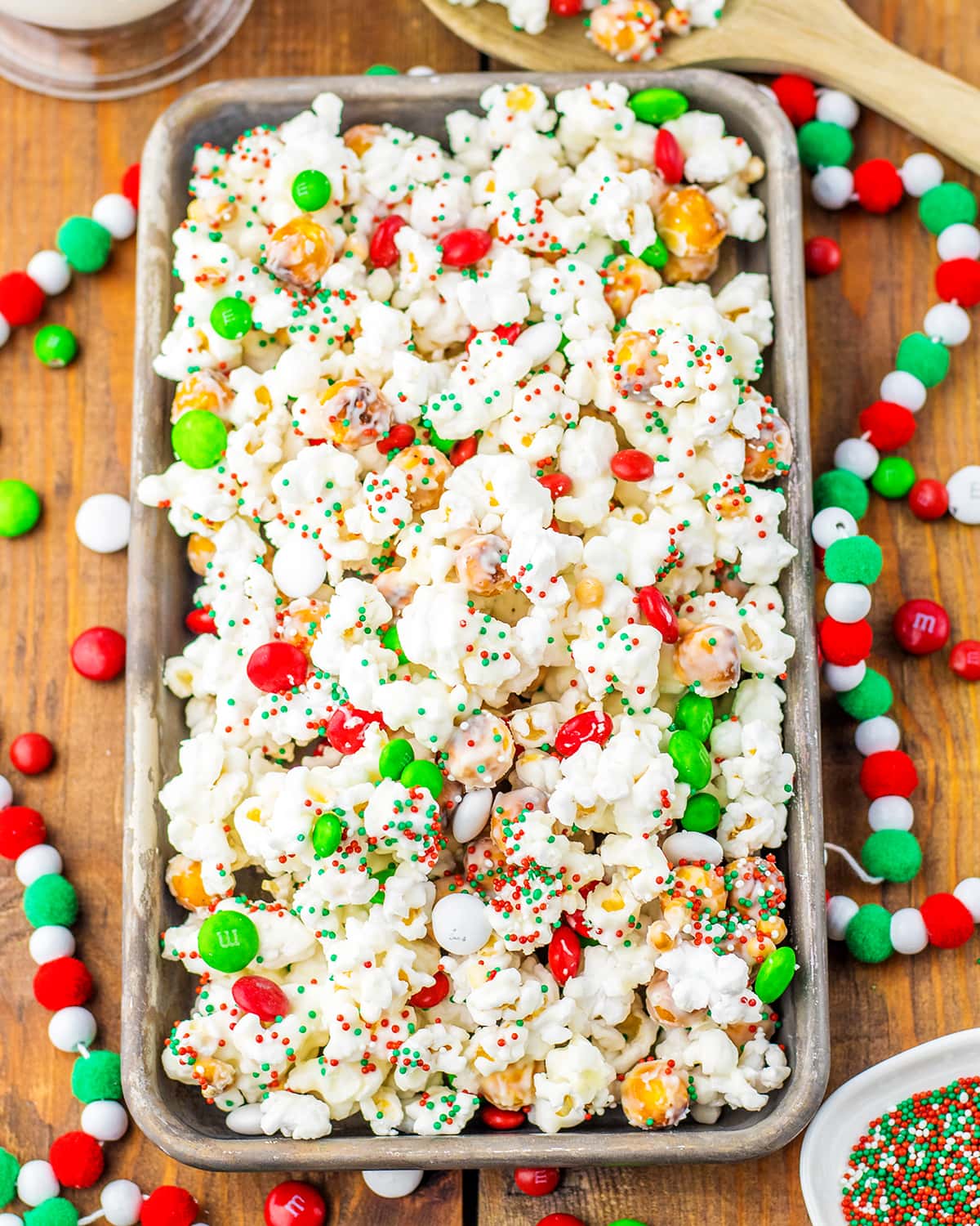 A pan of Christmas popcorn covered in white chocolate, and red, white and green round sprinkles.