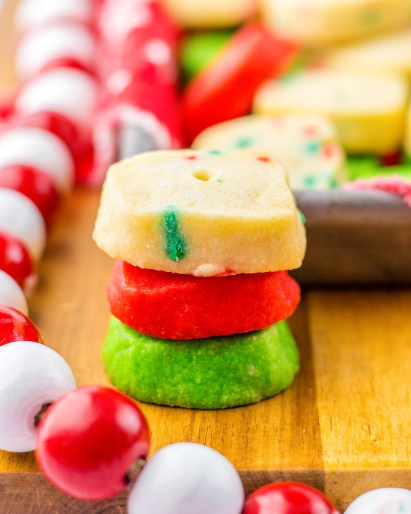 A stack of 3 mini christmas shortbread cookie bites. One is green, one is red, and one is white with sprinkles.