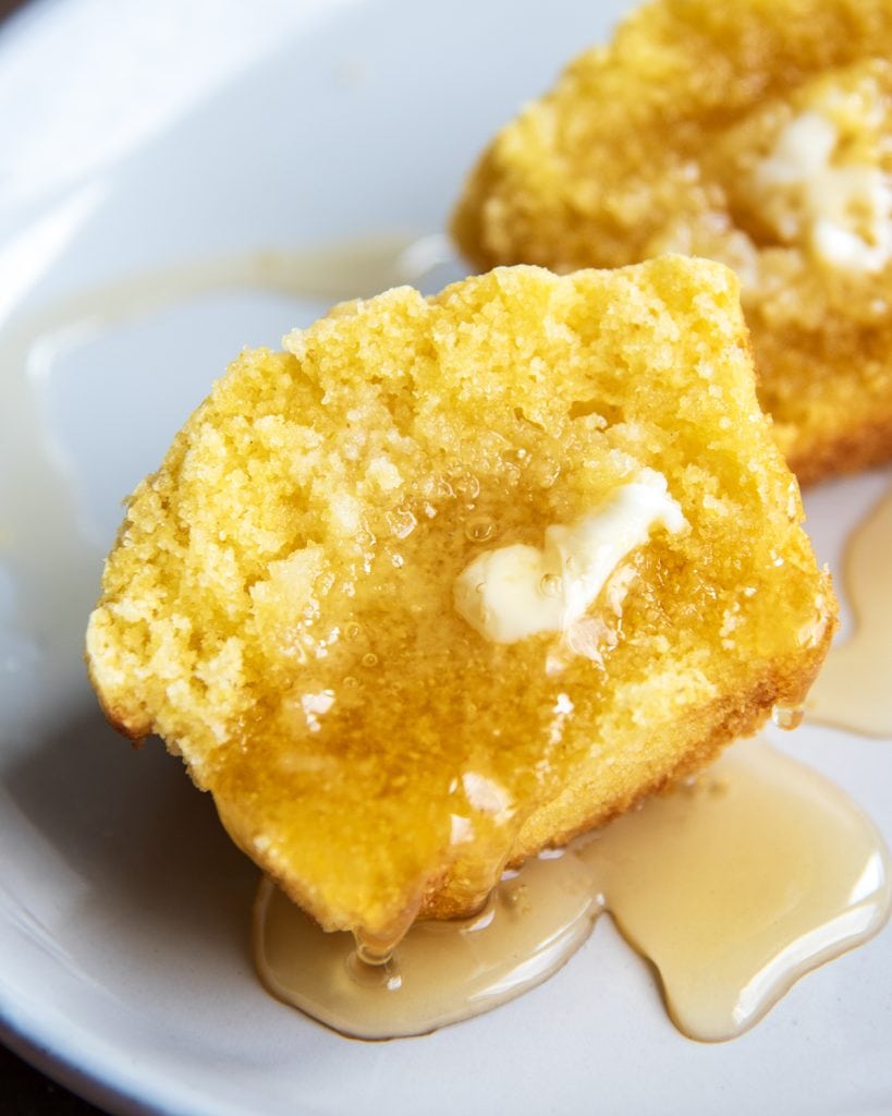 A cornbread muffin topped with butter and honey on a plate.